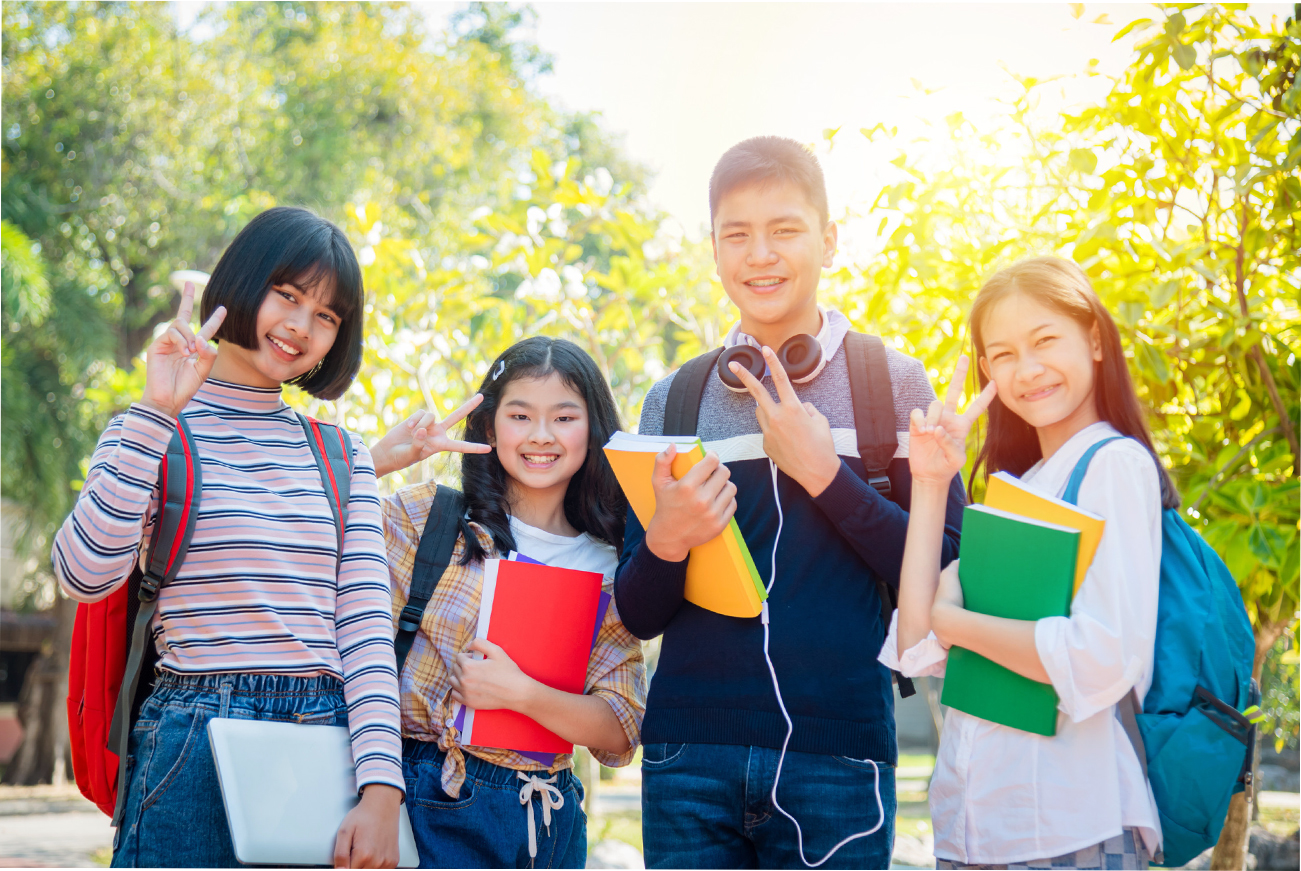 Four asian teenager students standing in park and smiling at camera